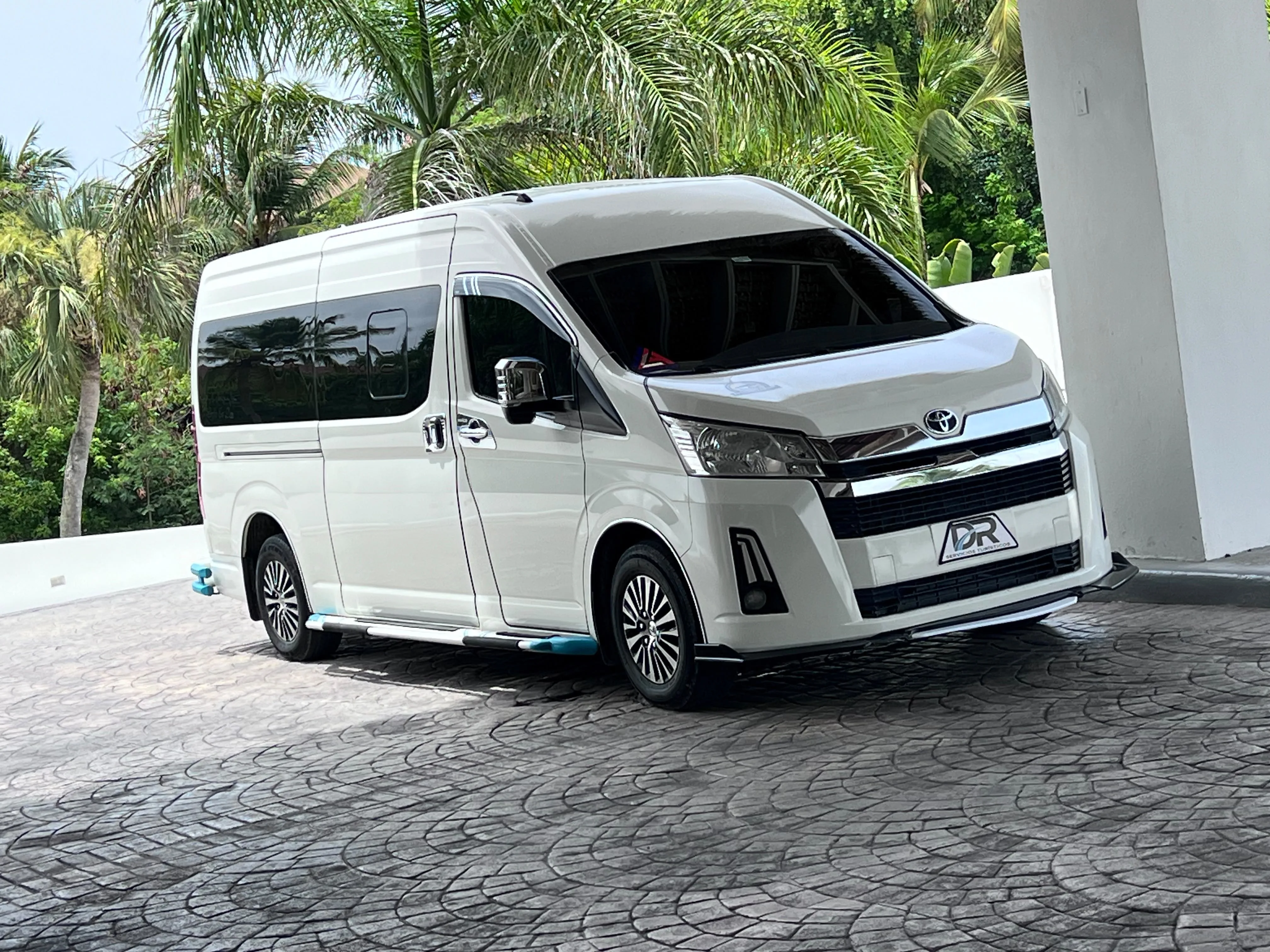 White minibus for private transfers of 11 to 15 passengers, parked beside a building.
